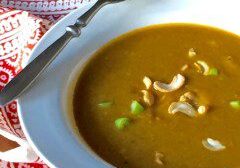 Bowl of creamy soup garnished with cashews and green herbs.