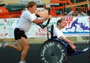 A man helping a woman lift a heavy barbell at a gym event.