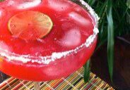 A vibrant red cocktail garnished with a lime slice and salt rim.
