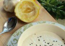 A bowl of creamy soup garnished with black sesame seeds, with garlic and lemon in the background.
