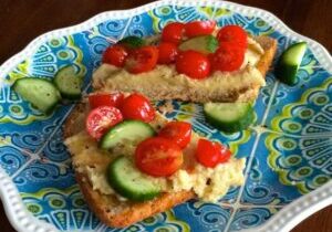 Open-faced sandwiches with cucumber and cherry tomatoes on a blue patterned plate.