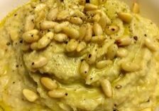 Close-up of creamy dip topped with pine nuts and seasoning.