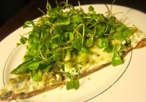 Open-faced sandwich topped with fresh greens and creamy spread.