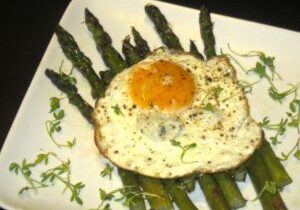 Grilled asparagus topped with a sunny-side-up egg on a white plate.