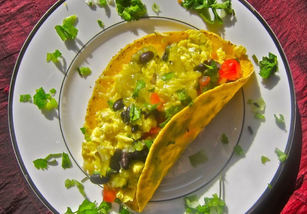 A vibrant taco filled with scrambled eggs, vegetables, and herbs on a decorated plate.
