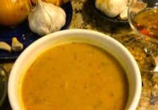 A bowl of creamy pumpkin soup with garlic and pumpkins in the background.