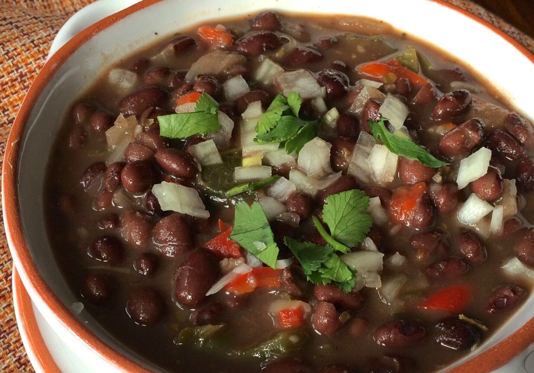A bowl of black bean soup garnished with fresh herbs and diced onions.
