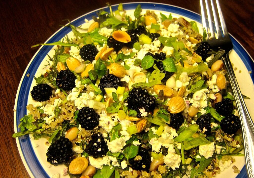 A fresh salad with blackberries, nuts, and greens on a colorful plate.