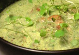 Creamy green soup garnished with fresh herbs in a dark bowl.