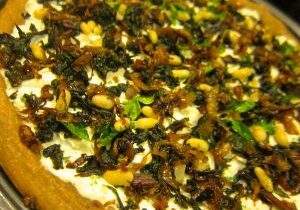 Close-up of a savory tart topped with herbs, nuts, and greens.