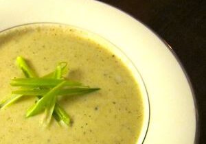 Creamy green soup garnished with fresh herbs in a white bowl.