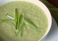 A bowl of creamy green soup garnished with fresh green herbs.