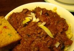 A bowl of chili topped with cheese, served with cornbread.