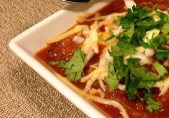 A bowl of rich red soup garnished with cheese and fresh cilantro.