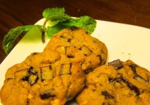 Two chocolate chip cookies on a white plate with a mint garnish.