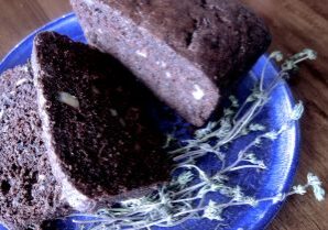 Sliced chocolate loaf cake on a blue plate with herbs.