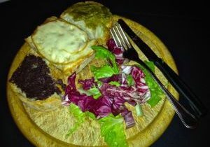 A wooden plate with fried eggs, salad, and utensils.