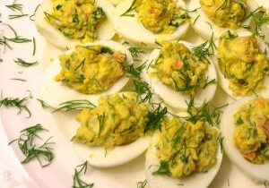 Deviled eggs garnished with fresh dill on a white plate.