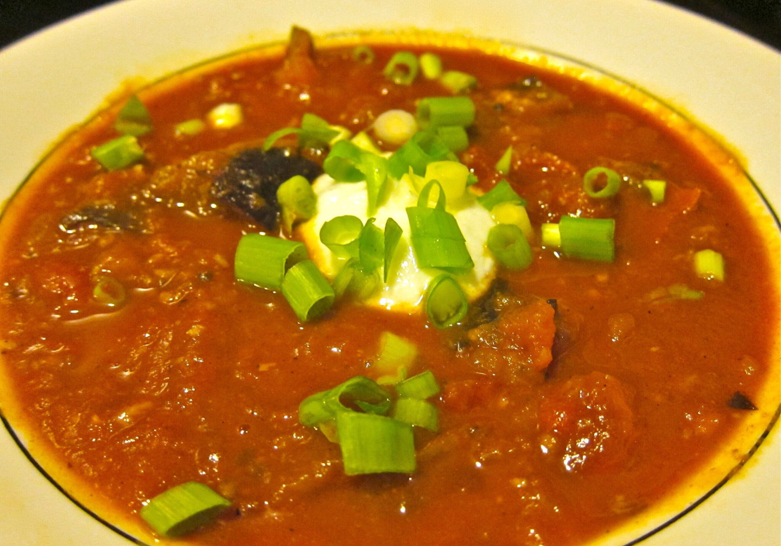A bowl of hearty chili topped with sour cream and green onions.