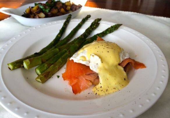 Eggs Benedict with smoked salmon and asparagus spears on a white plate.