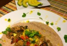 A plate with a tortilla topped with cooked vegetables and meat, garnished with herbs.
