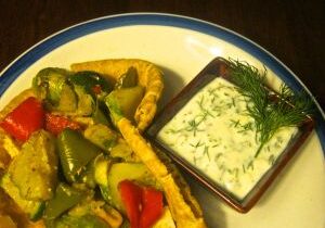 Plate of vegetable curry with a side of creamy herb sauce.