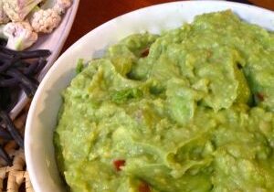 A bowl of fresh guacamole with tortilla chips and black beans.