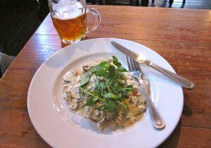 Plate of creamy pasta with herbs and a glass of beer on a wooden table.