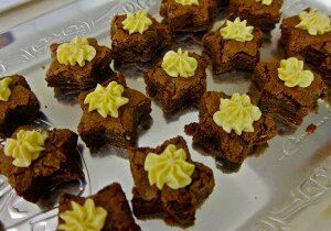 Star-shaped brownies topped with swirls of yellow frosting on a white tray.