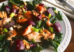 Salad with salmon, olives, and greens on a white plate.