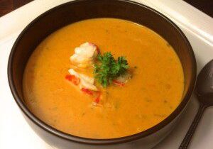 Creamy lobster bisque garnished with herbs in a black bowl.