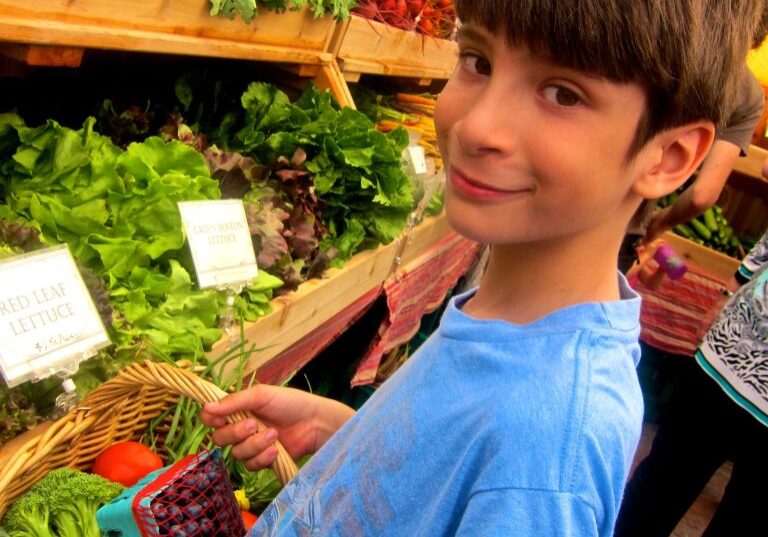 A smiling boy holding fresh produce at a market.