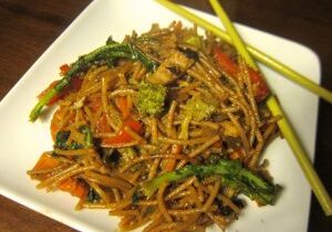 Plate of stir-fried noodles with vegetables and chopsticks.