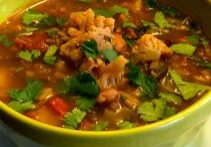 A bowl of hearty vegetable and lentil soup garnished with fresh herbs.