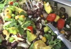 A colorful bowl of mixed bean salad with avocado and tomatoes.