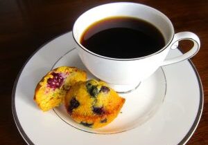 A cup of black coffee with two blueberry muffins on a white plate.