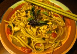 A bowl of spicy noodle soup with herbs and chopsticks.
