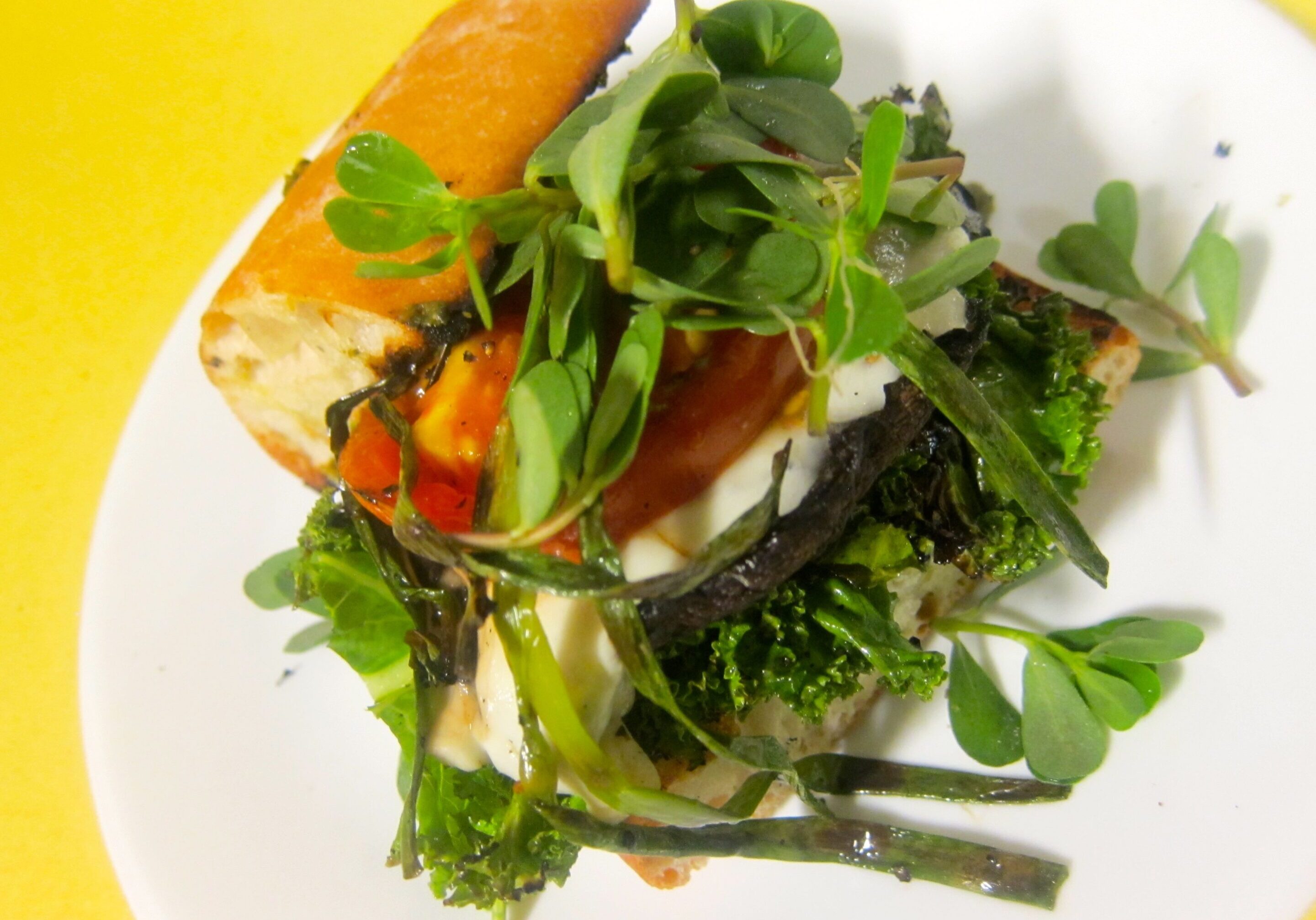 Fresh green salad with bread and colorful vegetables on a white plate.