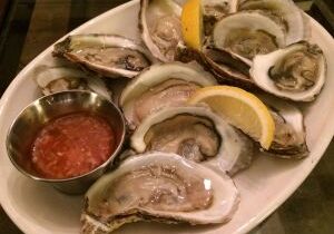 Fresh oysters served on a platter with lemon wedges and cocktail sauce.