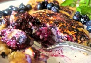 Close-up of a blueberry pancake with syrup and fresh blueberries.