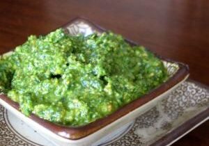 A bowl of vibrant green chutney on a patterned surface.