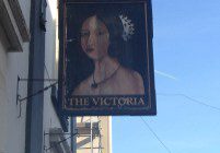 Signboard of 'The Victoria' pub with a painted portrait of a woman.