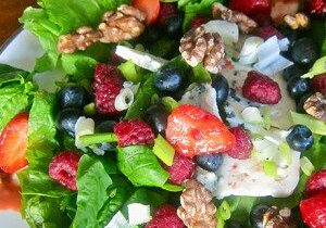 Colorful fresh fruit and nut salad with greens and berries.