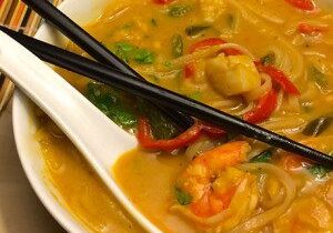 A bowl of shrimp noodle soup with chopsticks and a spoon.
