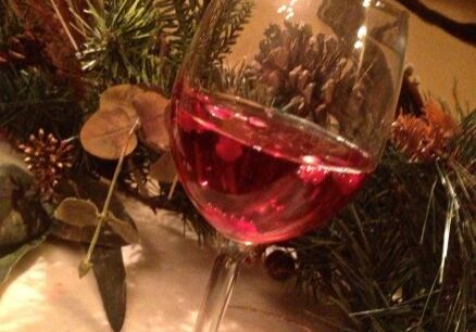 A glass of red wine with festive decorations in the background.