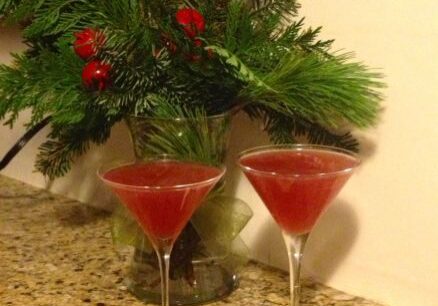Two red cocktails with festive greenery and a bowl of guacamole on the side.