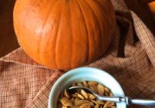 A pumpkin and a bowl of roasted pumpkin seeds on a cloth.