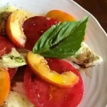 Tomato, peach, basil salad on white plate.