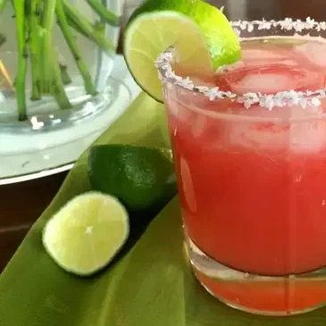 Red cocktail with lime and salted rim.