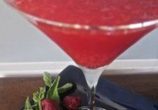 A vibrant red cocktail in a martini glass garnished with a cherry.